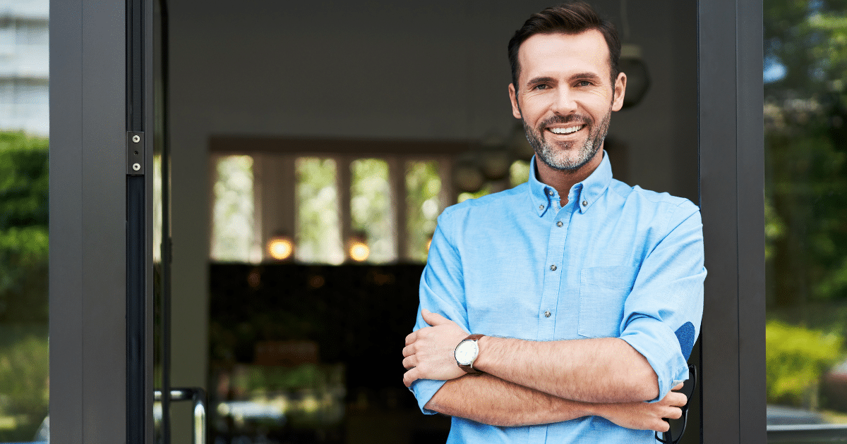 Smiling businessman standing at the entrance, representing business loans and cash advances for entrepreneurs.