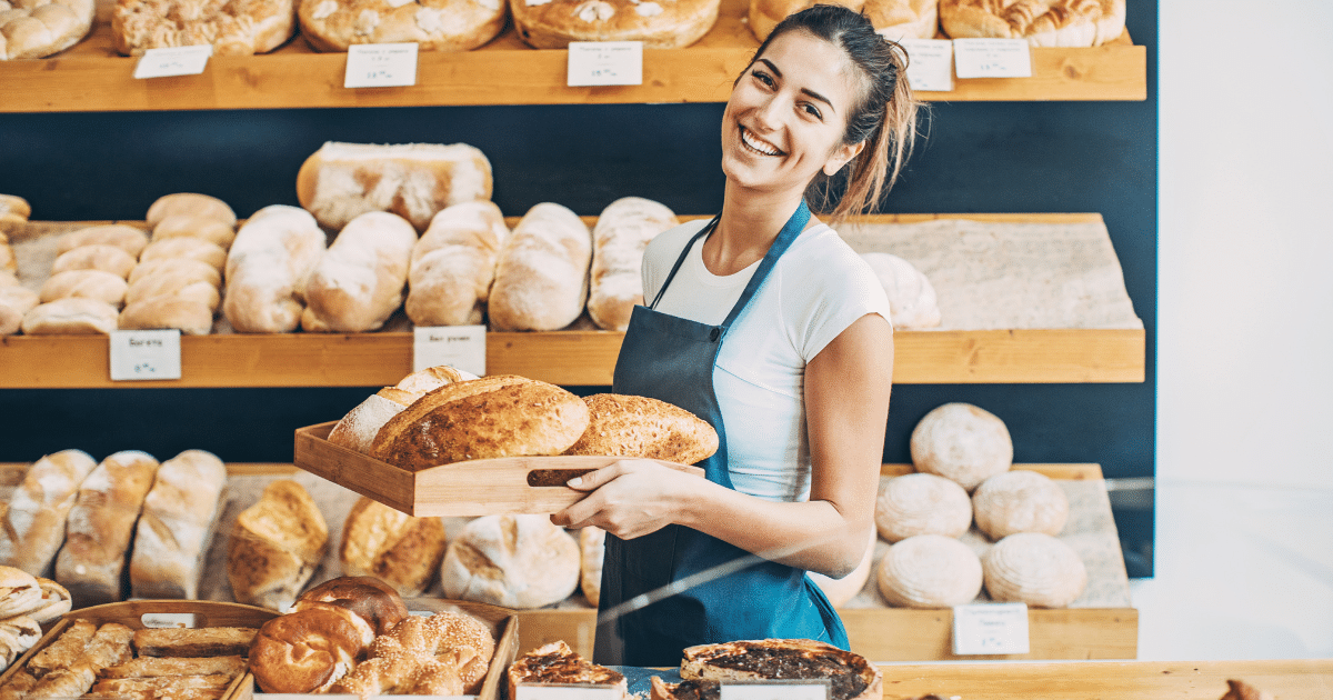 Smiling bakery owner holding fresh bread in a shop, showcasing small business success and growth opportunities.