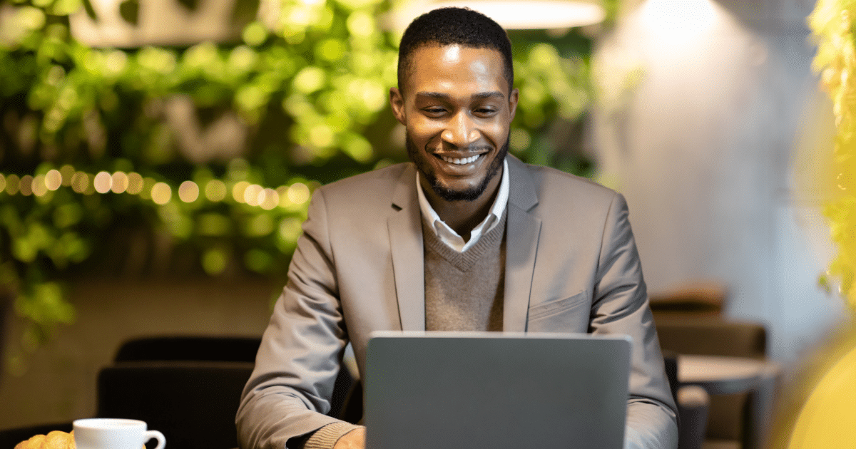 Smiling businessman using a laptop in a cafe, exploring Facebook marketing strategies for small business growth.