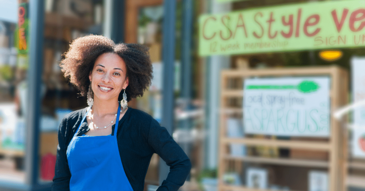 Smiling small business owner in front of a store promoting local produce and holiday shopping strategies.