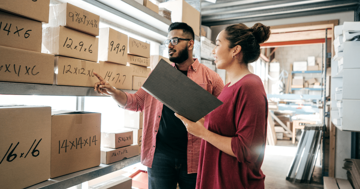 Two business professionals discussing inventory management in a warehouse, highlighting franchise growth and funding opportunities.