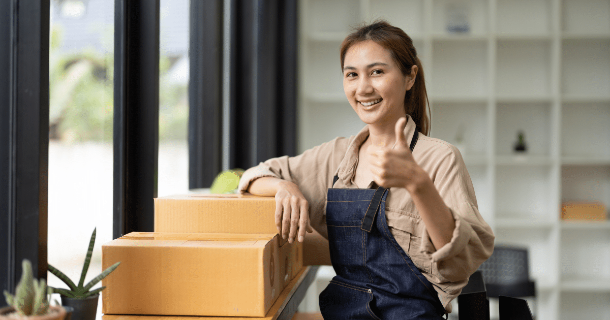 Smiling woman giving a thumbs up next to boxes, representing growth in pharmacy and medical equipment businesses.