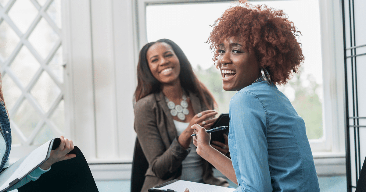 Two women smiling and engaging in a discussion, representing teamwork and support in financial recovery and credit repair strategies.