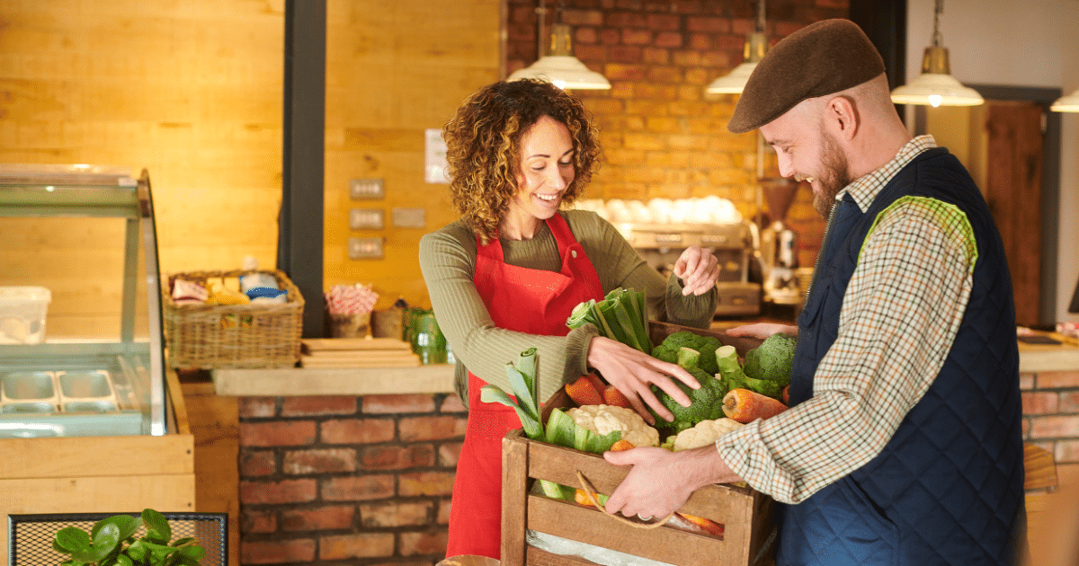 Smiling business owners exchanging fresh produce in a vibrant market, showcasing community networking and collaboration.