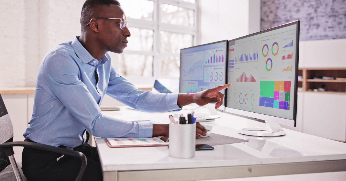 Business professional analyzing financial data on dual monitors, highlighting insights for effective decision-making.