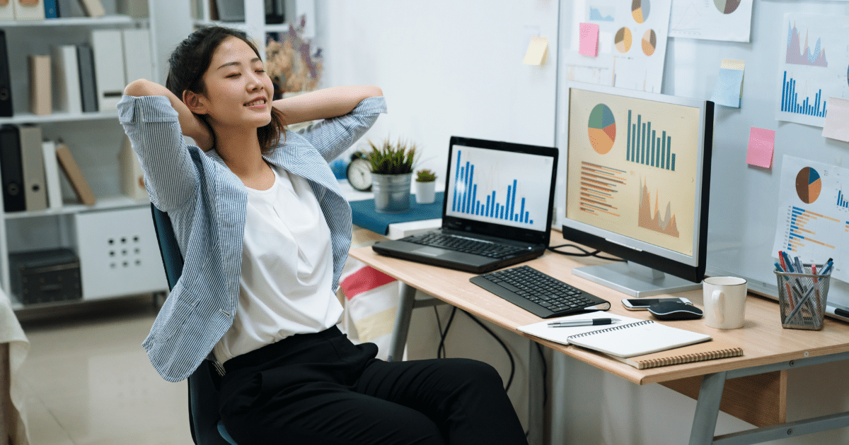 Businesswoman relaxing at desk with financial charts, highlighting factoring and invoice financing benefits for growth.