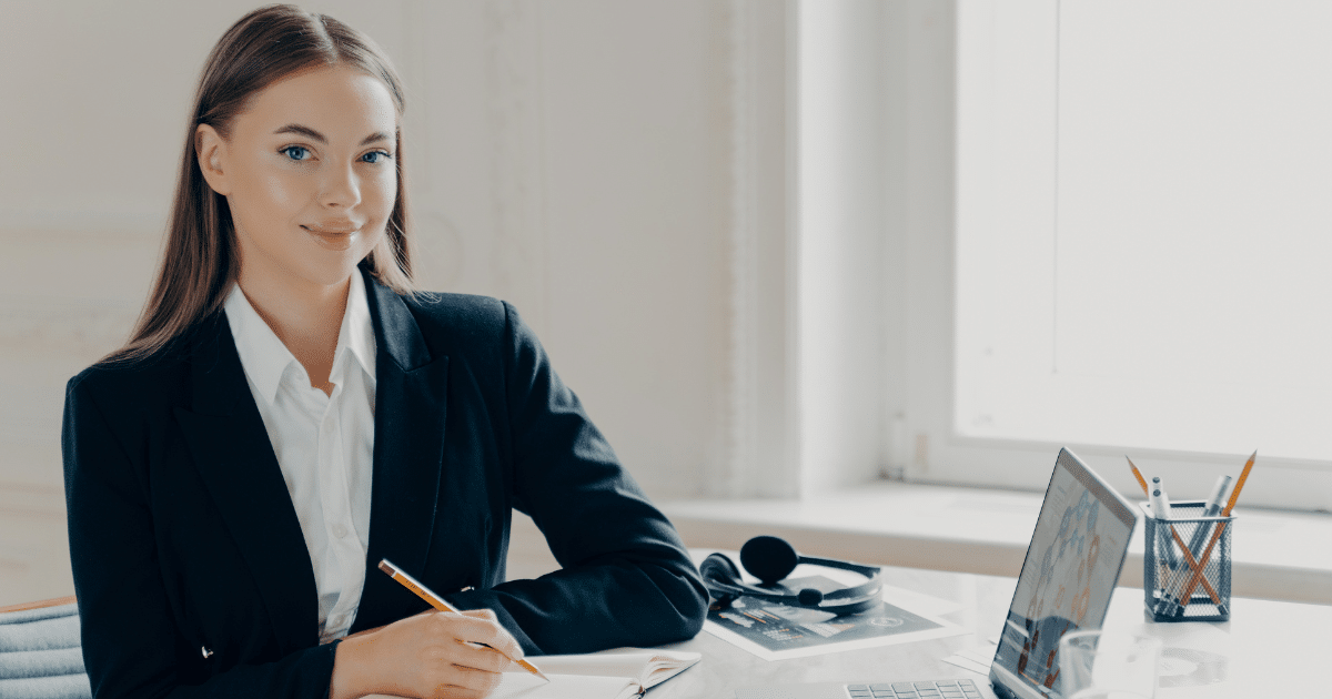 Professional woman at a desk with a laptop, notepad, and headphones, representing effective time management and productivity.