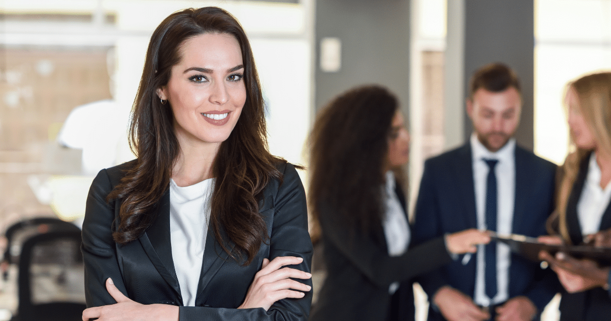 Business professional smiling confidently with colleagues discussing strategies in a modern office setting.
