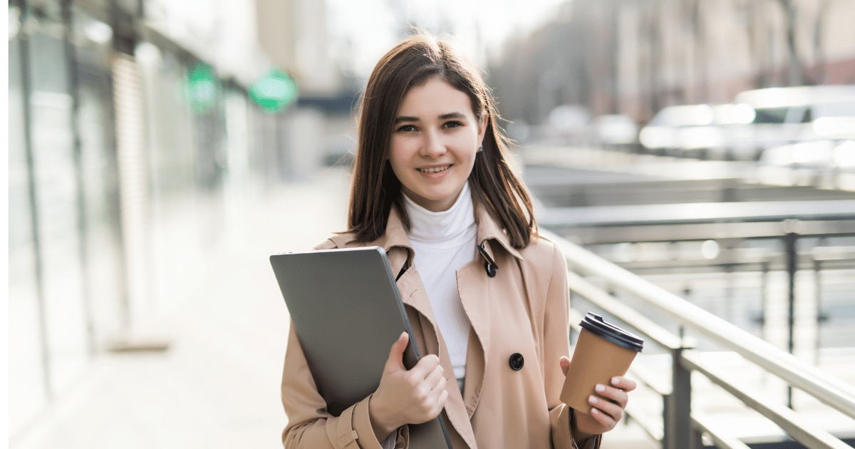 Young professional woman holding a laptop and coffee cup, ready to enhance her workday with office exercises.