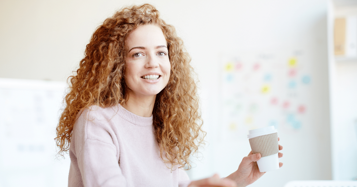 Smiling woman enjoying coffee in a workspace, representing effective stress relief techniques for busy workdays.