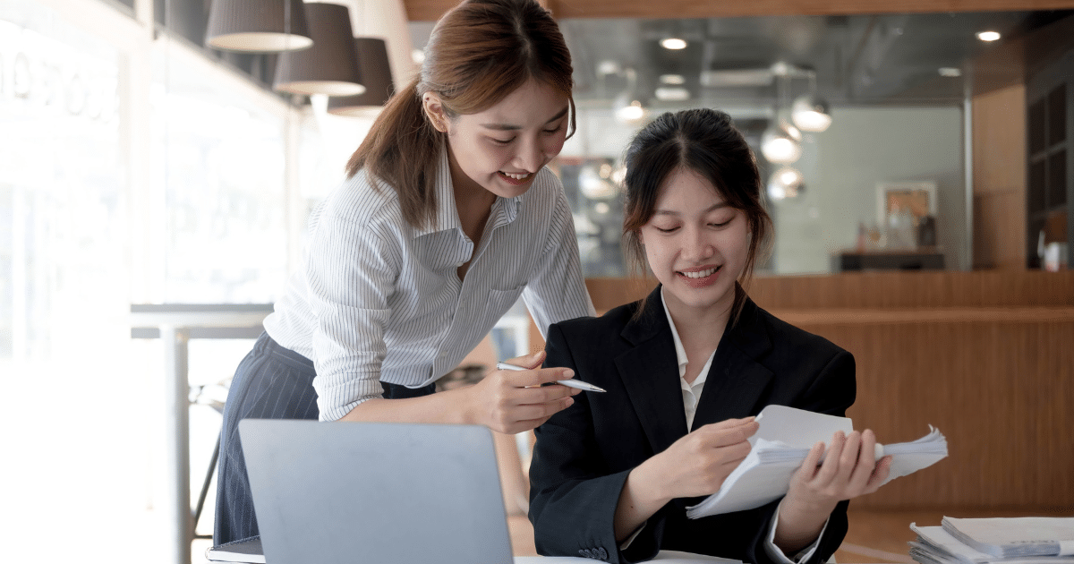 Two businesswomen discussing small business loan documents in a modern office setting, emphasizing collaboration and preparation.