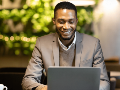 Smiling businessman using a laptop in a cafe, exploring Facebook marketing strategies for small business growth.