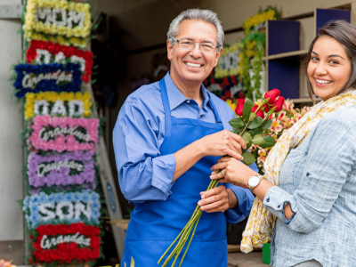 Smiling florist and customer holding roses in a flower shop, showcasing community support and business growth opportunities.