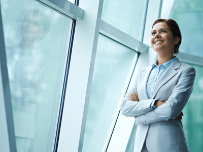 Business professional smiling by large windows, promoting office energy efficiency and savings strategies.