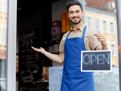 Smiling business owner holding an 'OPEN' sign, representing AFN's flexible cash advances for business growth.