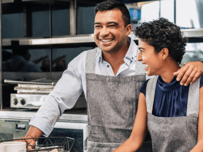 Smiling business owners in aprons discussing unsecured business loans for poor credit applicants in a cafe setting.