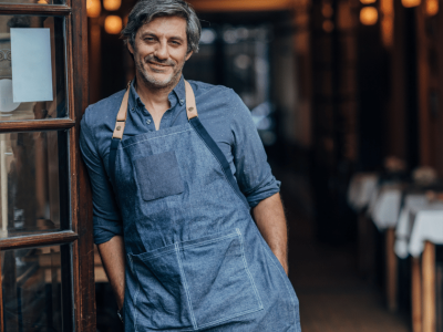 Smiling restaurant owner in apron, showcasing teamwork and leadership in business success and employee empowerment.