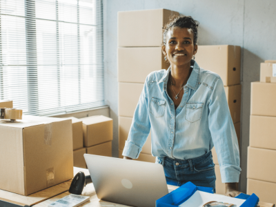 Smiling woman in a workspace with boxes and a laptop, representing optimized medical accounts receivable solutions.