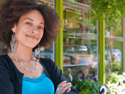 Smiling businesswoman in front of a shop, representing smart financing and networking for business growth.