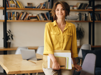 Businesswoman in a yellow shirt holding documents, representing financial empowerment and avoiding personal savings for business expenses.