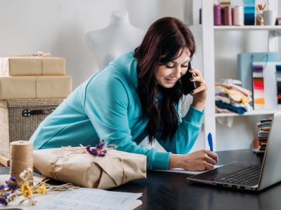 Small business owner managing finances and health care under Obamacare, surrounded by supplies and a laptop.