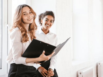 Two businesswomen smiling and discussing strategic holiday budgeting in a bright office setting.