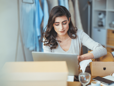 Woman working on a laptop in a cozy office, surrounded by boxes and office supplies, representing tailored medical financing solutions.