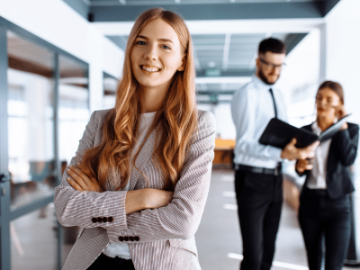 Professional woman smiling confidently in a modern office, showcasing business efficiency and teamwork with colleagues.