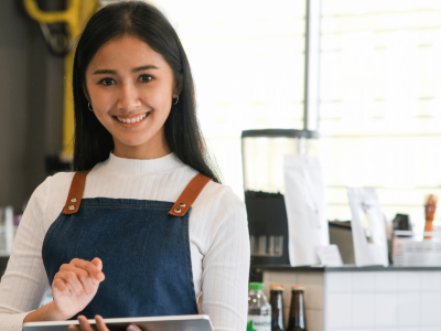 Smiling young woman in a cafe holding a tablet, representing small business growth and profit potential strategies.