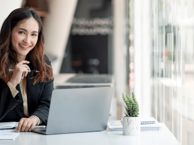Professional woman smiling at a desk with a laptop, pen, and office supplies, representing affordable office equipment upgrades.