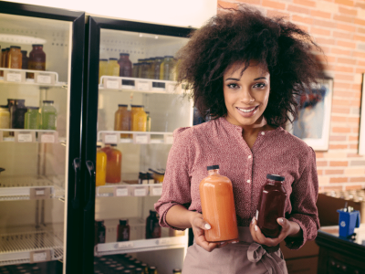 Smiling woman holding juice bottles in a small business, showcasing cost-cutting strategies for entrepreneurs.