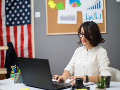 Businesswoman working on a laptop in an office with financial charts, preparing for a small business loan or credit application.