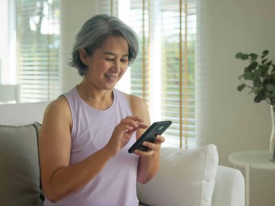 Asia adult people middle age happy relax old woman using mobile ask AI chatGPT chat bot look health care app sit at home sofa elder aging asian aged female. Online social media smart pay order system.